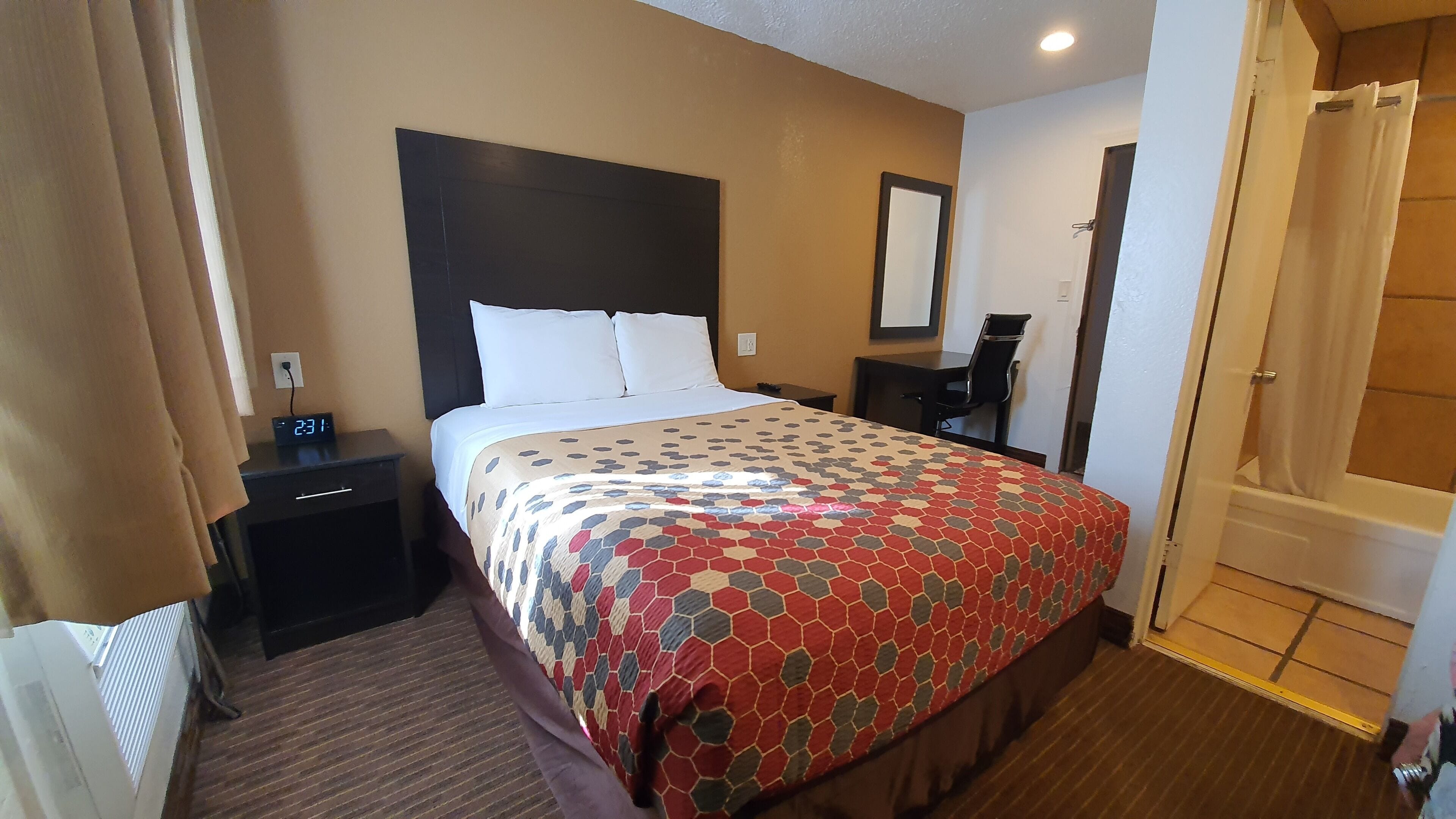 A hotel room with a bed, a nightstand, a desk, a chair, a mirror, and a door leading to a bathroom.