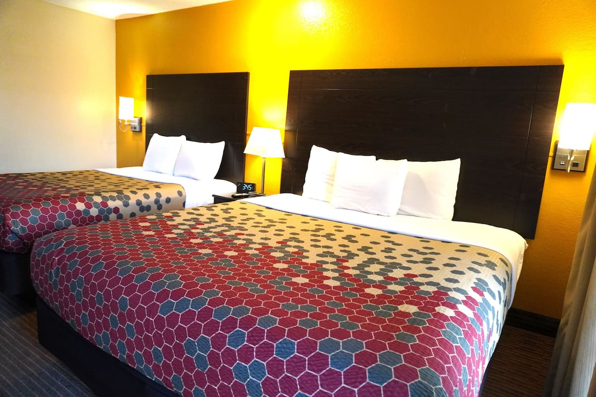 Habitación de hotel con dos camas, cada una con colcha estampada, lámparas de noche y un reloj en la mesita.