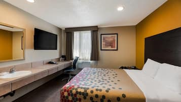 A hotel room with a bed, a desk, a chair, a sink, a mirror, a flat-screen TV, and a window with curtains.