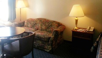 Una habitación con un sofá floral, una mesa redonda, una lámpara y un teléfono sobre una mesita de noche.