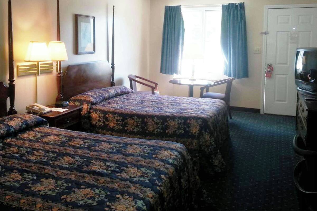 A hotel room with two beds, a desk, a chair, a lamp, and a television.