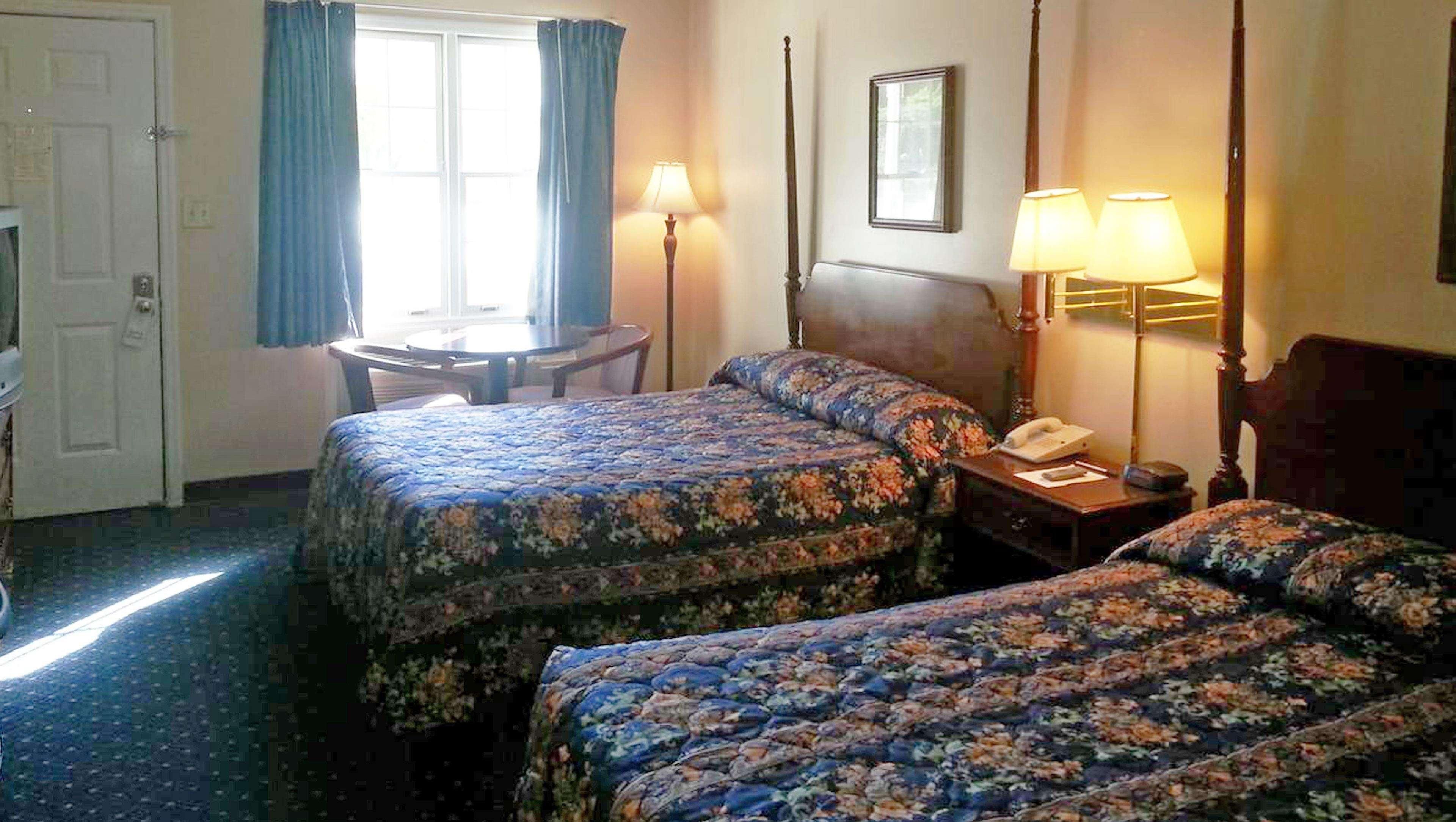 Habitación de hotel con dos camas, un escritorio, una silla y dos lámparas de noche.