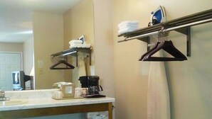 A bathroom with a sink, a mirror, a towel rack, a coffee maker, and a hanging clothes rack.
