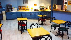 A dining area with blue cabinets, yellow tables, and black chairs.