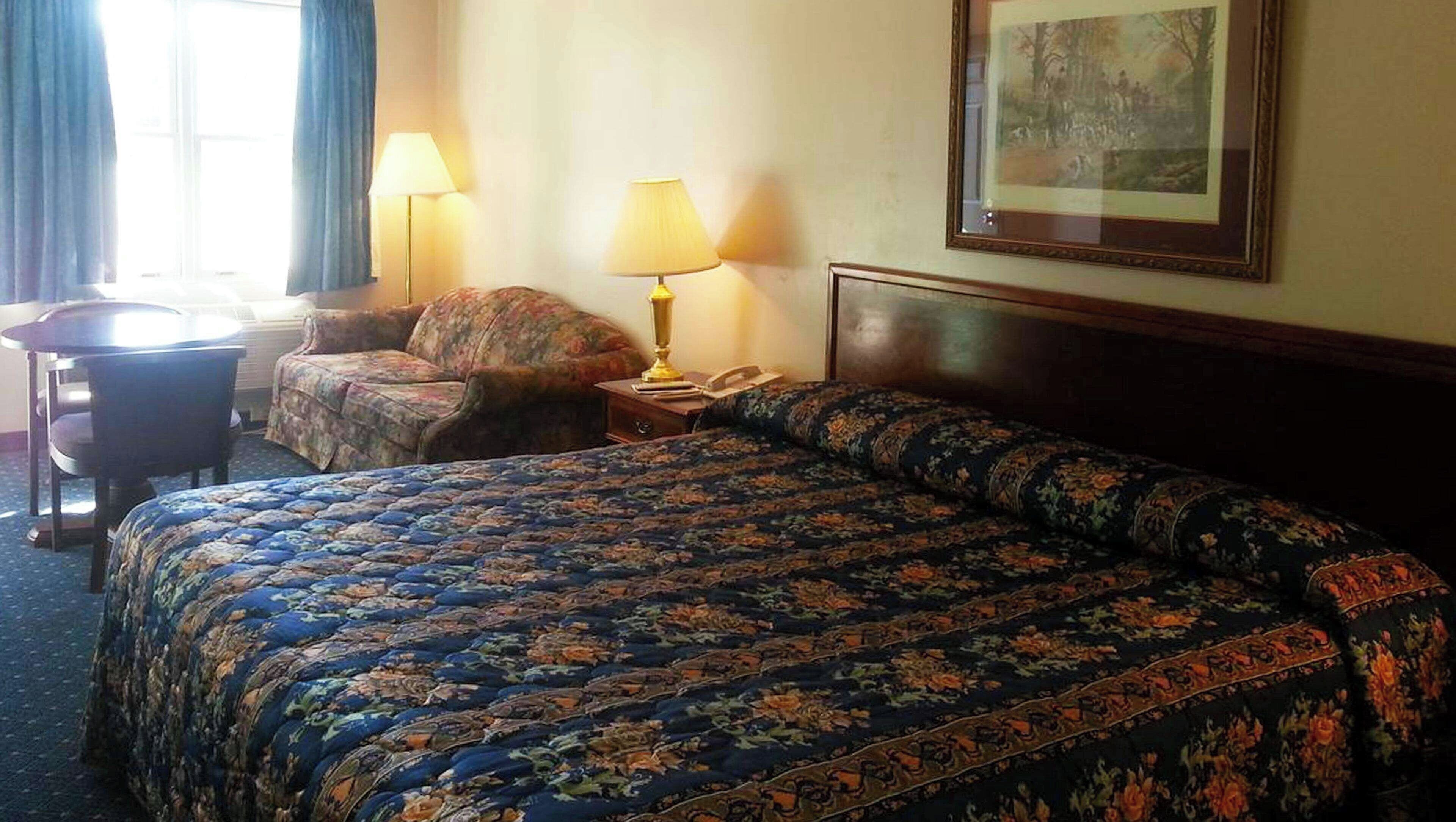 Een hotelkamer met een groot bed, een stoel, een bureau, twee lampen en een ingelijst schilderij aan de muur.