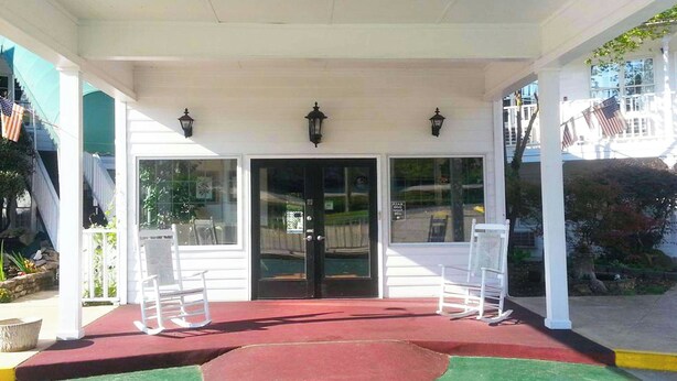 A covered porch with a red carpet, white chairs, and two black lanterns. - Stratford Motor Inn East Ellijay (Ellijay)