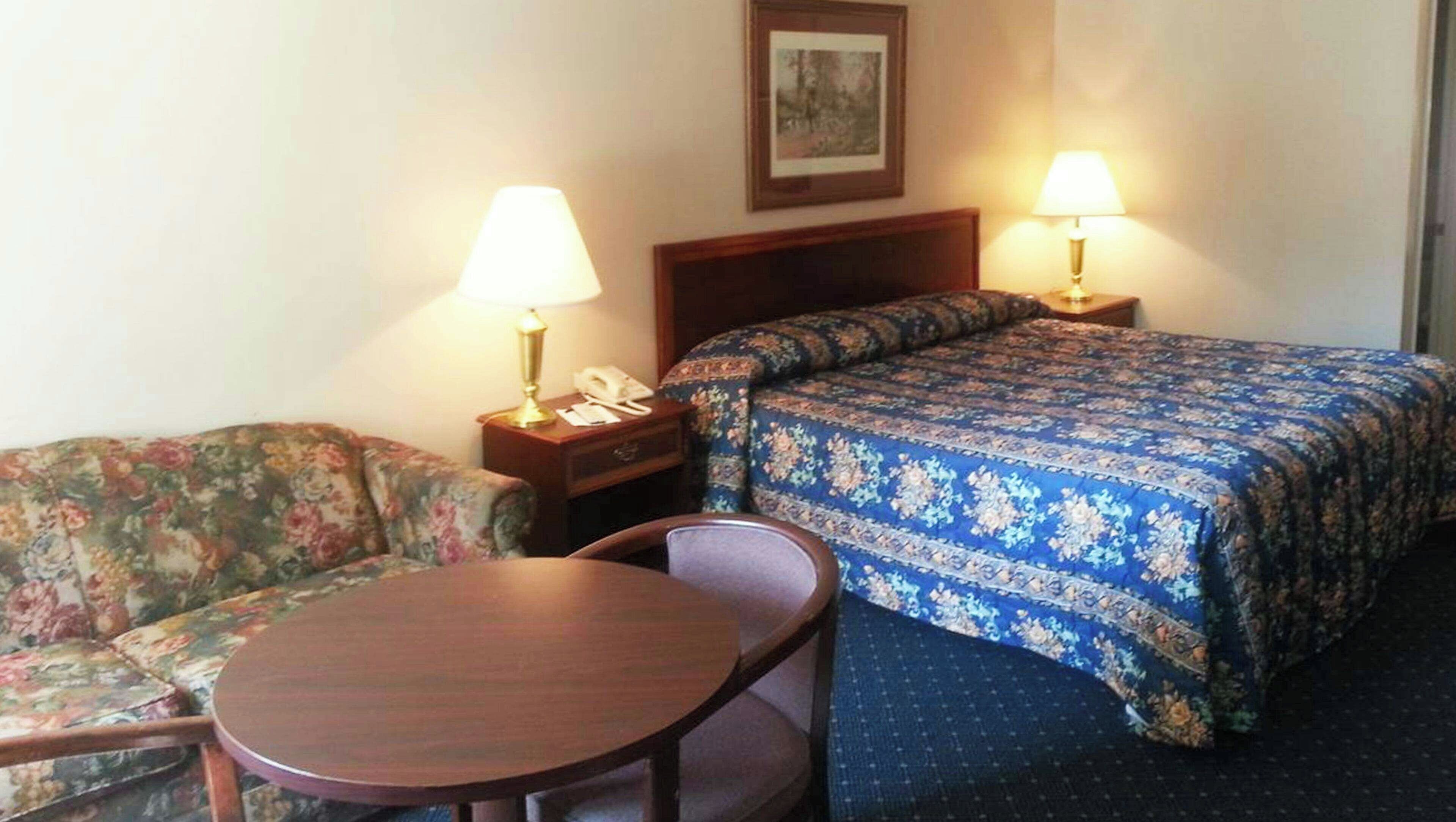 A hotel room with a bed, a sofa, a table, and two bedside lamps.