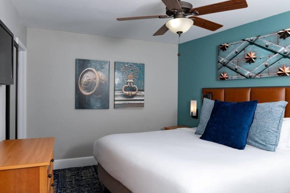 A bedroom with a bed, a ceiling fan, and two wall-mounted artworks.