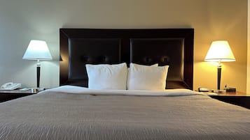 A hotel room with a large bed, two bedside lamps, a headboard, and a nightstand with a phone and a notepad.