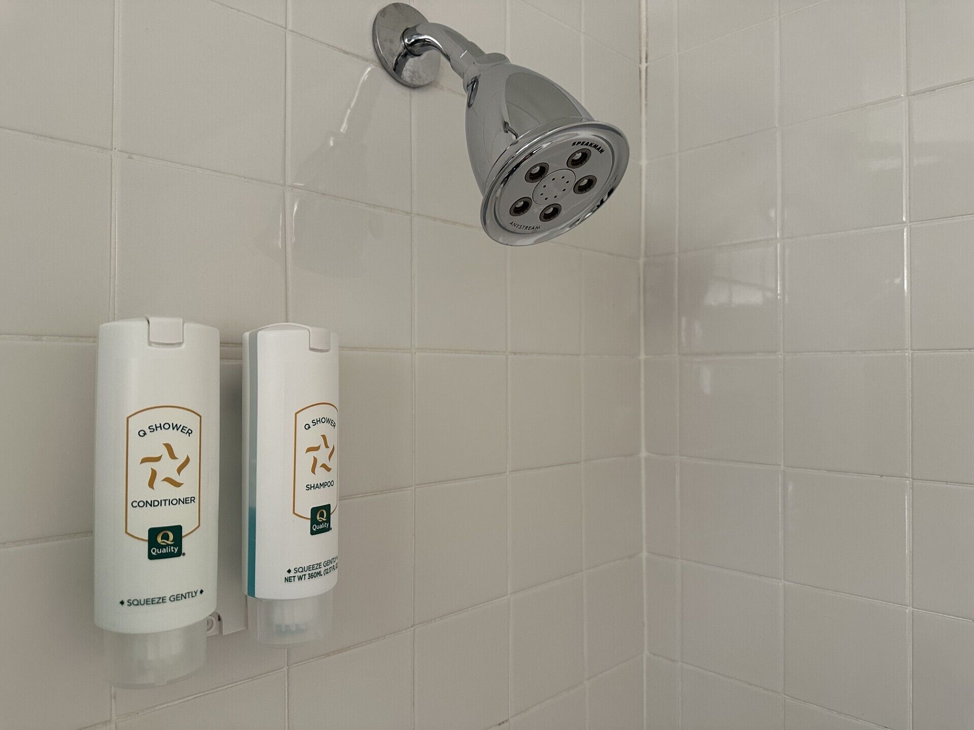 Chuveiro com chuveiro manual e dois frascos de condicionador e shampoo Q Shower.