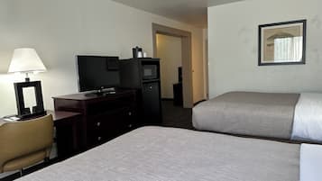 Una habitación de hotel con dos camas, un escritorio con lámpara, televisor, microondas y un cuadro en la pared.