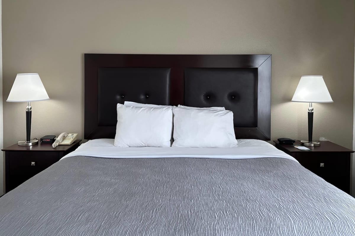 A hotel room with a large bed, two bedside tables, a telephone, and two lamps.