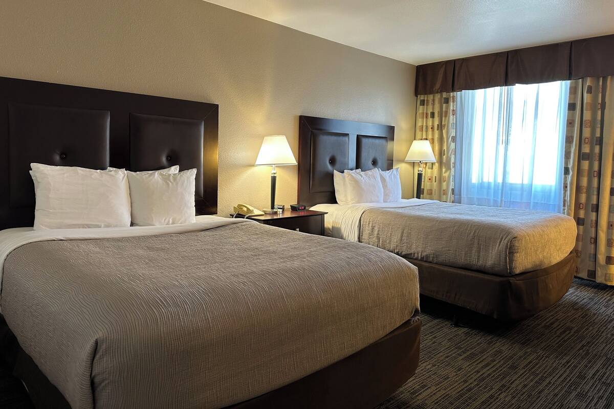 A hotel room with two beds, a nightstand with a lamp, and a window with curtains.