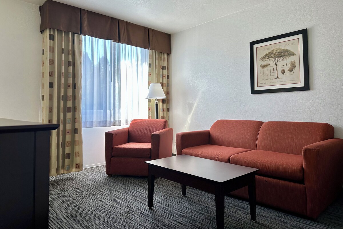 Ein Hotelzimmer mit Sofa, Sessel, kleinem Tisch, Lampe und einem gerahmten botanischen Druck an der Wand.