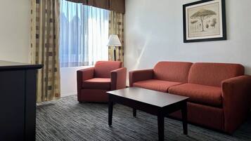 A hotel room with a sofa, armchair, small table, lamp, and a framed botanical illustration on the wall.