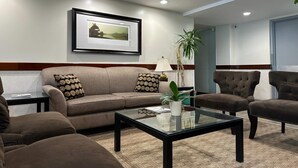 Ein Wohnzimmer mit einer Couch, Sesseln, einem Couchtisch, einem gerahmten Bild an der Wand und einer Topfpflanze.