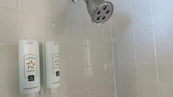 Une douche équipée d’un pommeau amovible et de deux flacons de shampoing et d’après-shampoing fixés au mur.