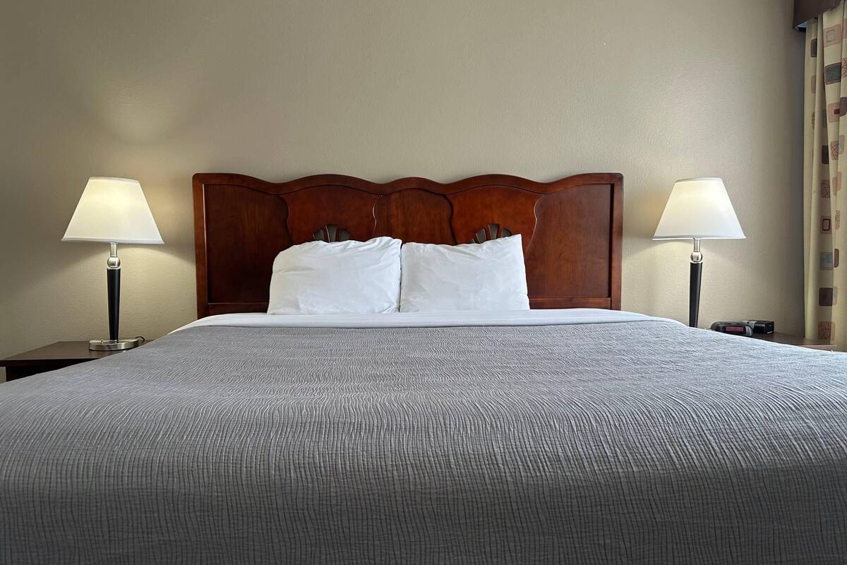 A neatly made bed with a wooden headboard, two bedside lamps, and a plain wall.