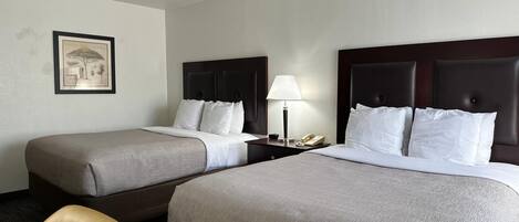 Habitación de hotel con dos camas, una mesita de noche con lámpara, teléfono y un cuadro en la pared.