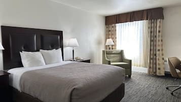 Hotelkamer met een groot bed, nachtkastje, lamp, stoel en raam met gordijnen.