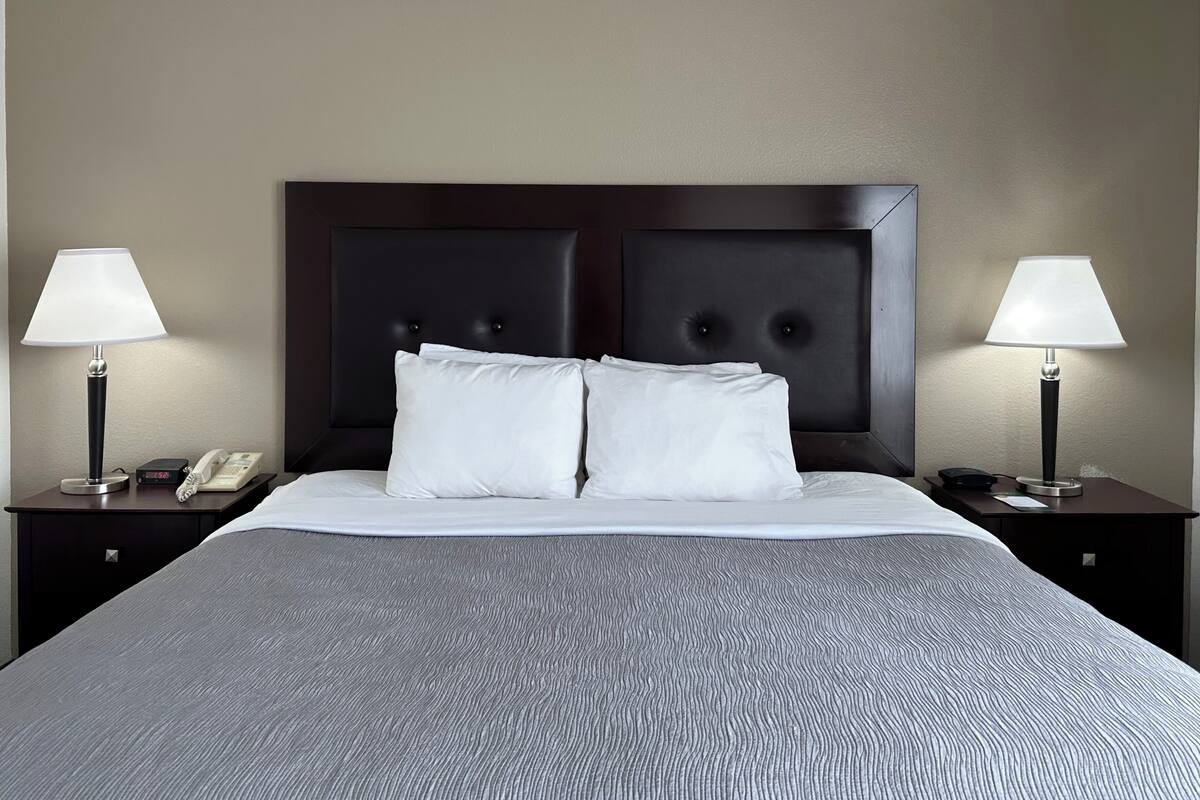 A hotel room with a large bed, two bedside tables, a telephone, and two lamps.