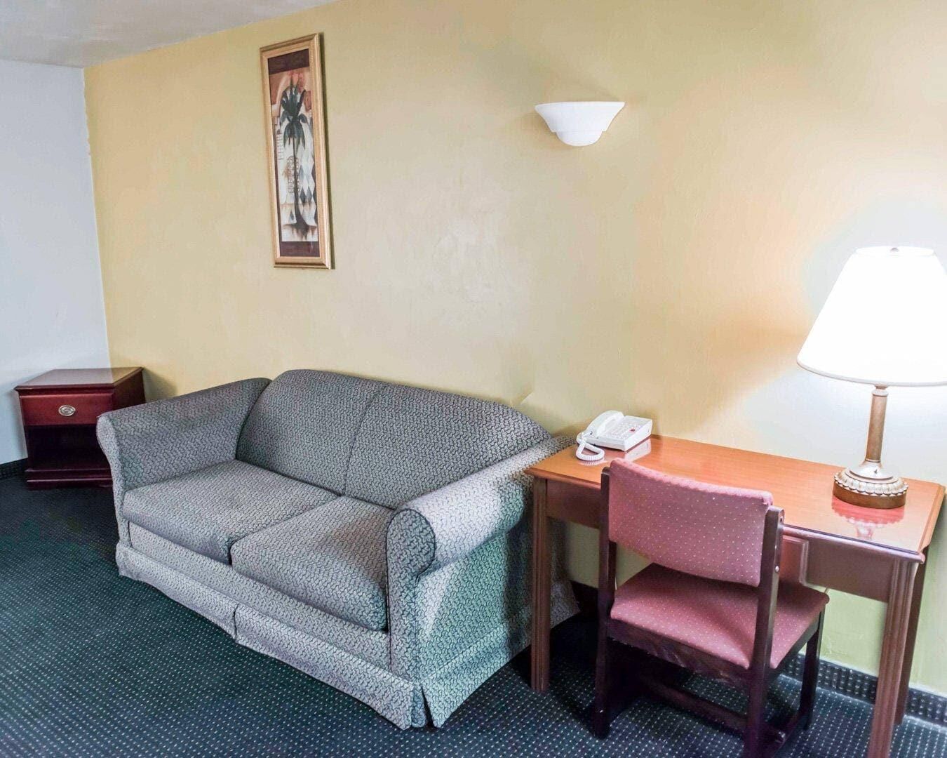 A room with a sofa, a wooden desk with a telephone and lamp, a small red cabinet, and a wall-mounted light fixture.