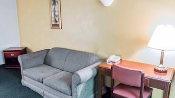A room with a sofa, a wooden desk with a telephone and lamp, a small red cabinet, and a wall-mounted light fixture.