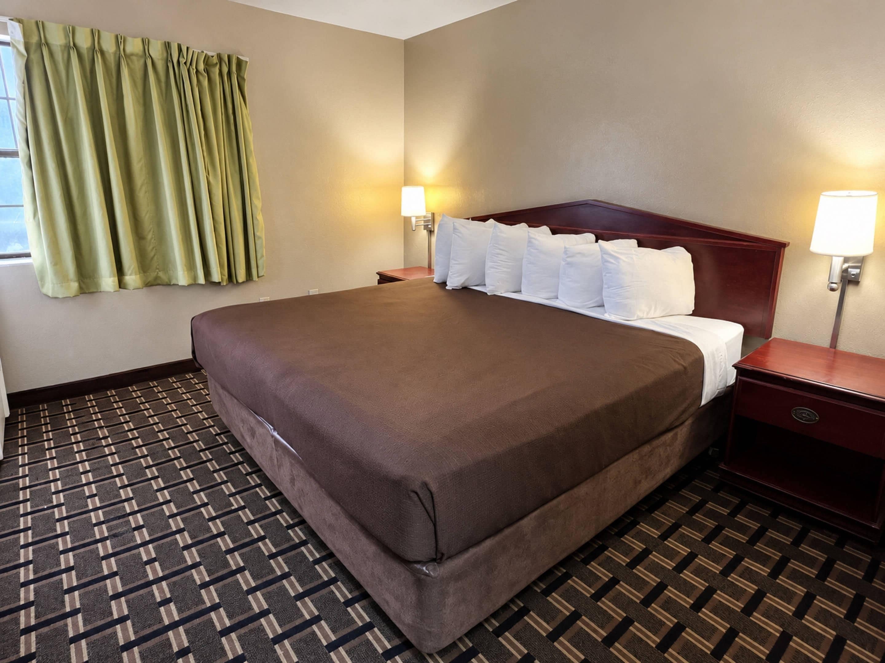 A hotel room with a large bed, two bedside tables, a window with curtains, and a patterned carpet.