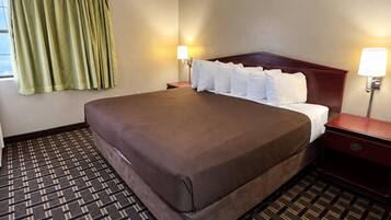 A hotel room with a large bed, two bedside tables, a window with curtains, and a patterned carpet.
