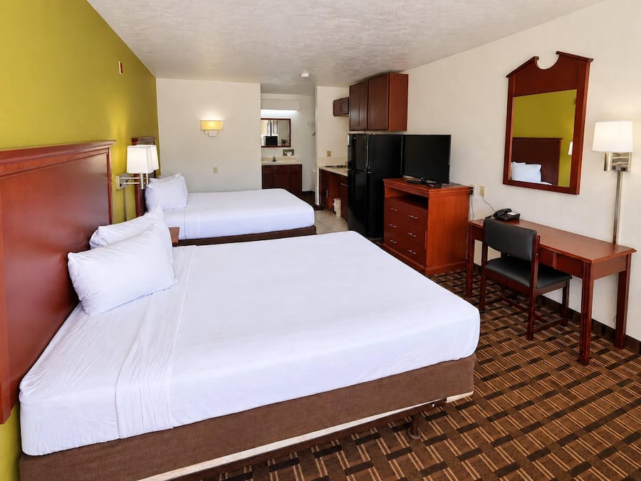 A hotel room with two beds, a desk, a refrigerator, a television, and a mirror.