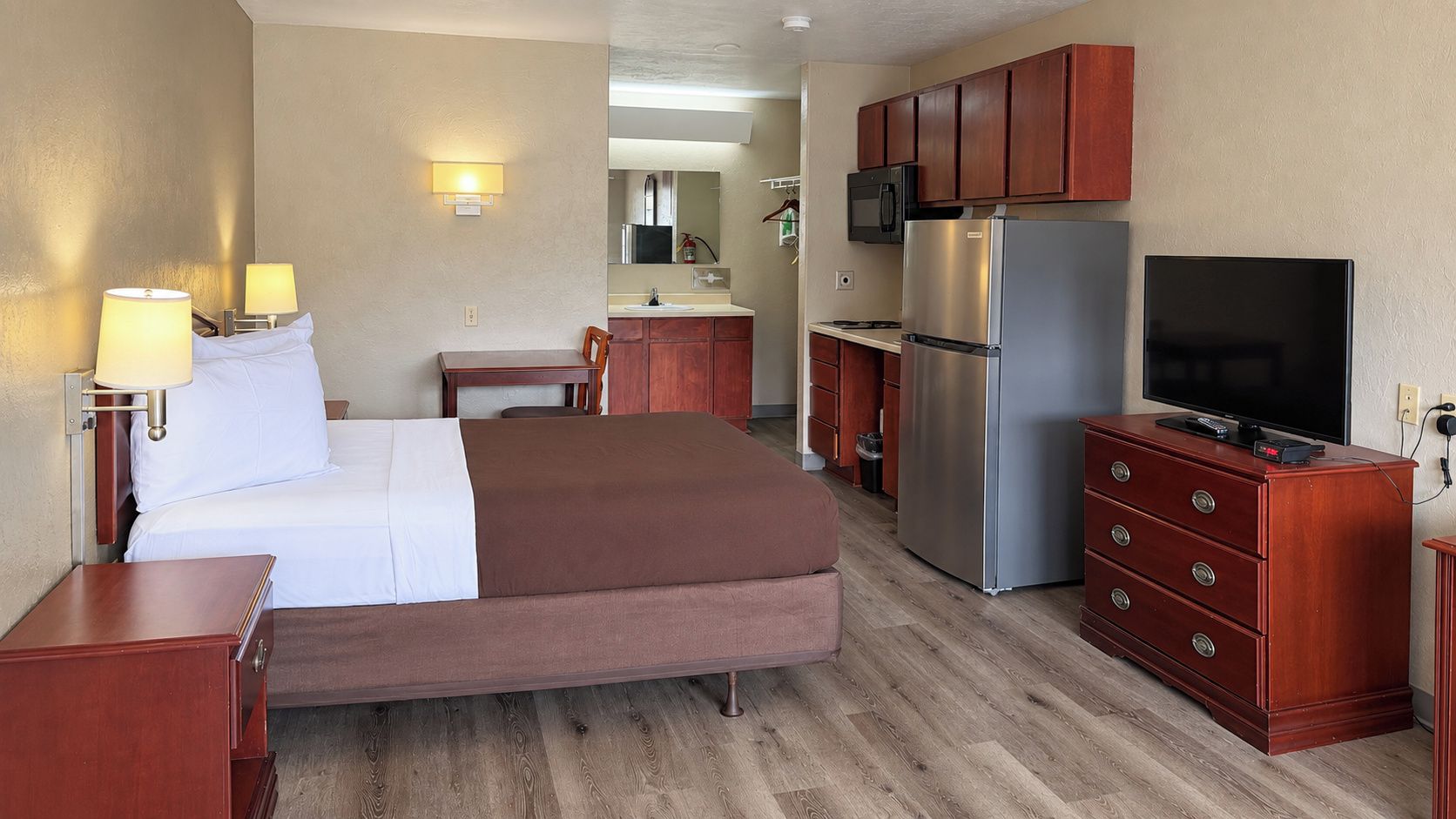 A hotel room with a bed, bedside lamps, a television, a refrigerator, and a microwave.
