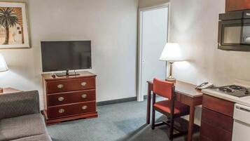 Camera d'albergo compatta con divano, TV, scrivania con lampada, forno a microonde e fornelli.