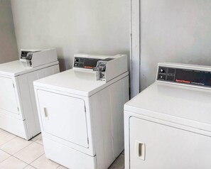 Trois sèche-linge commerciaux blancs, alignés contre un mur uni.
