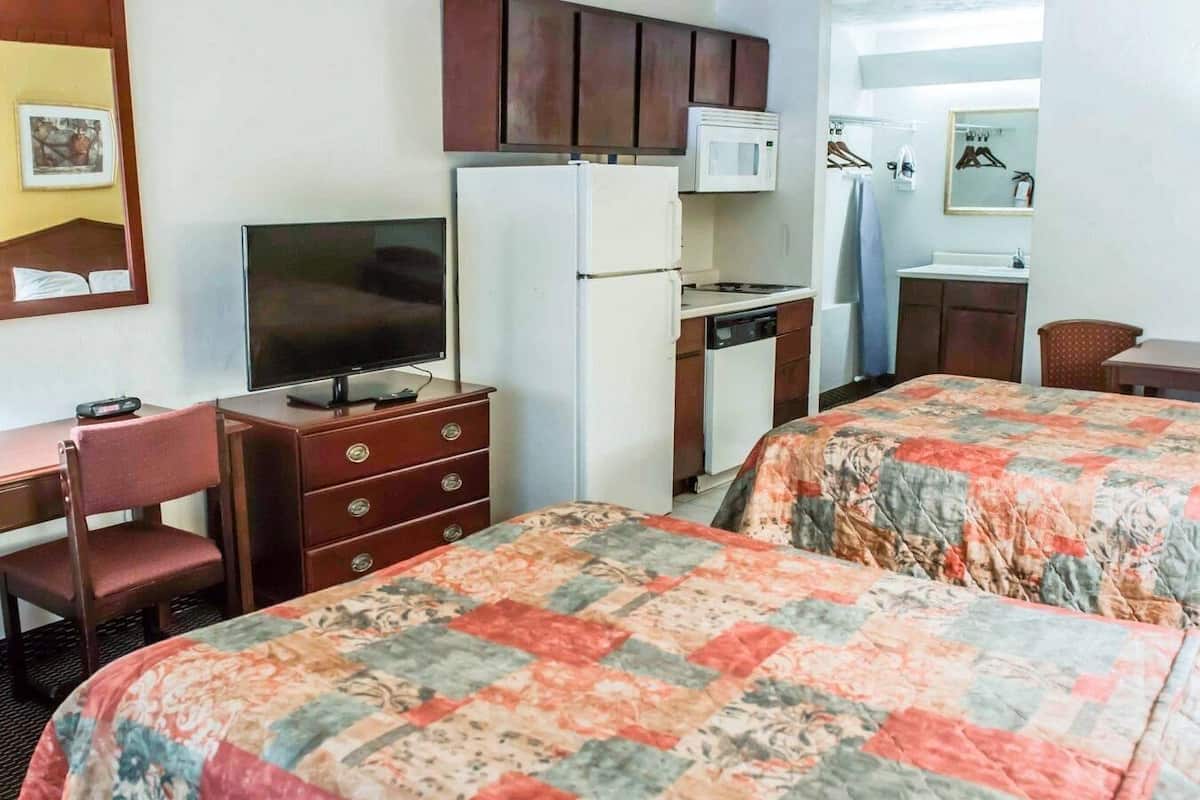 A hotel room with a TV, a refrigerator, a microwave, a small kitchen area, a desk with a chair, and two beds with floral bedding.