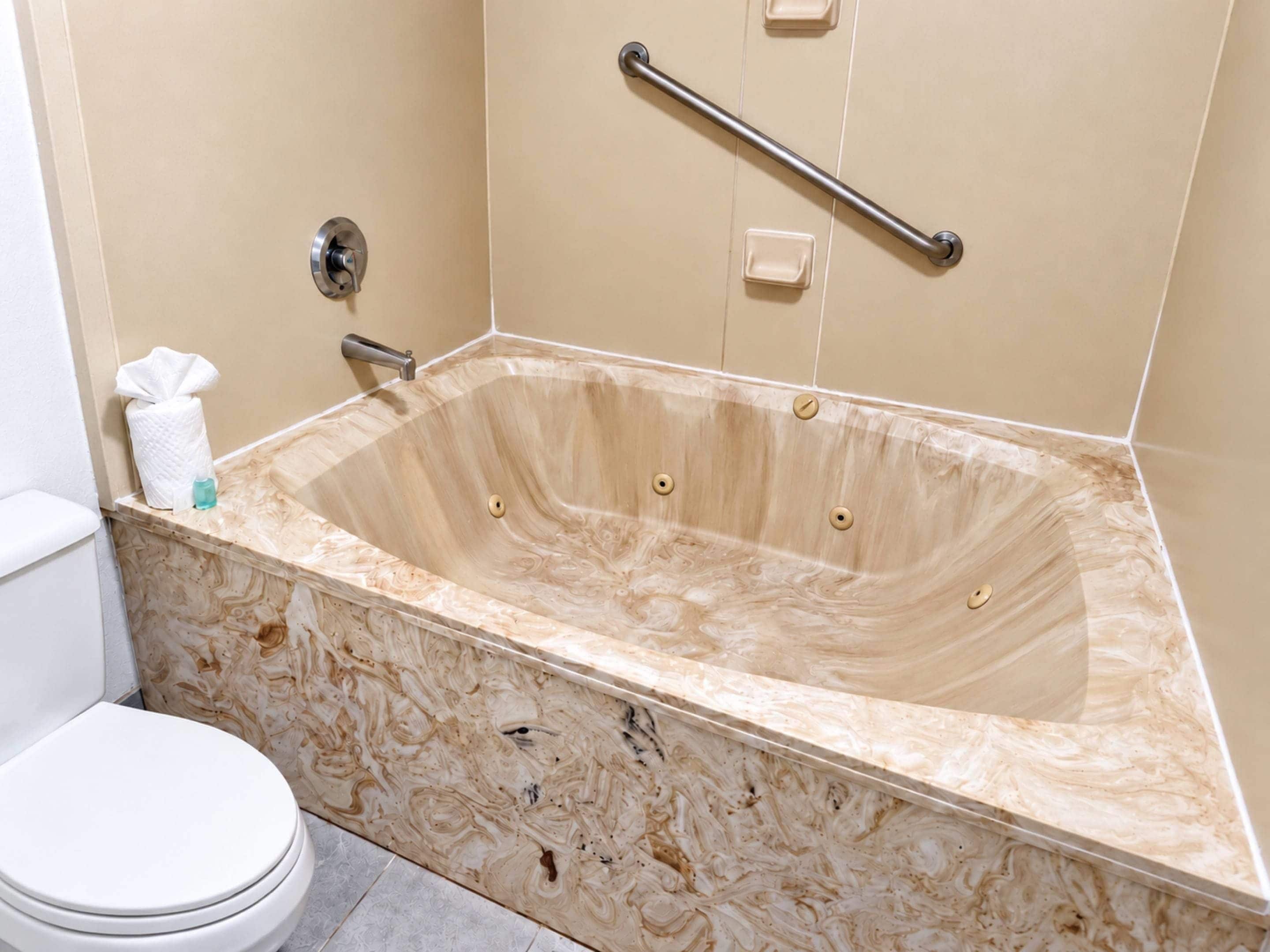 A bathroom with a marble bathtub, a toilet, and a handrail.