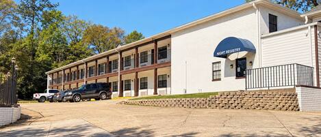 A two-story motel with a night registry sign, a parking lot, and a stone wall.
