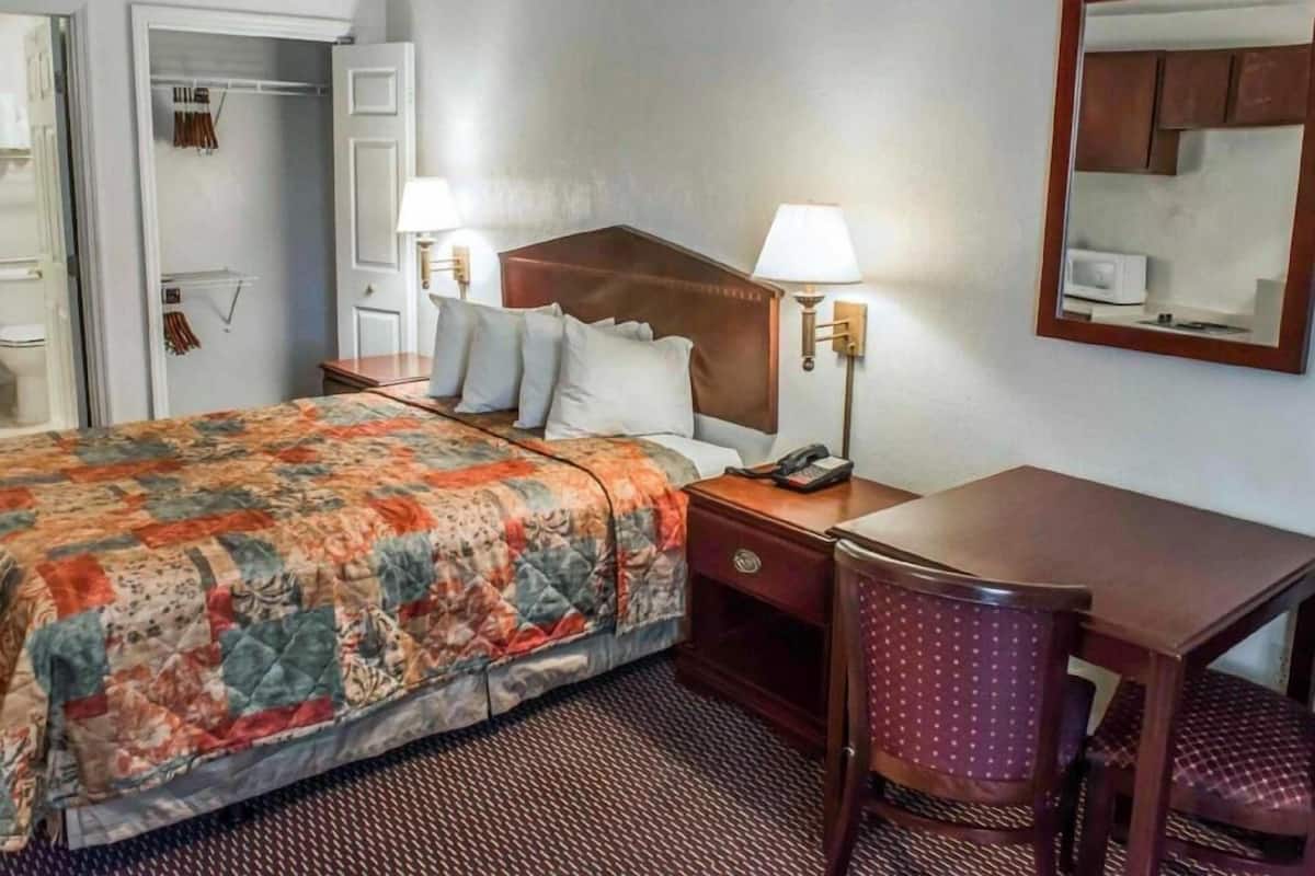 A hotel room with a bed, bedside table, chair, and a mirror on the wall.