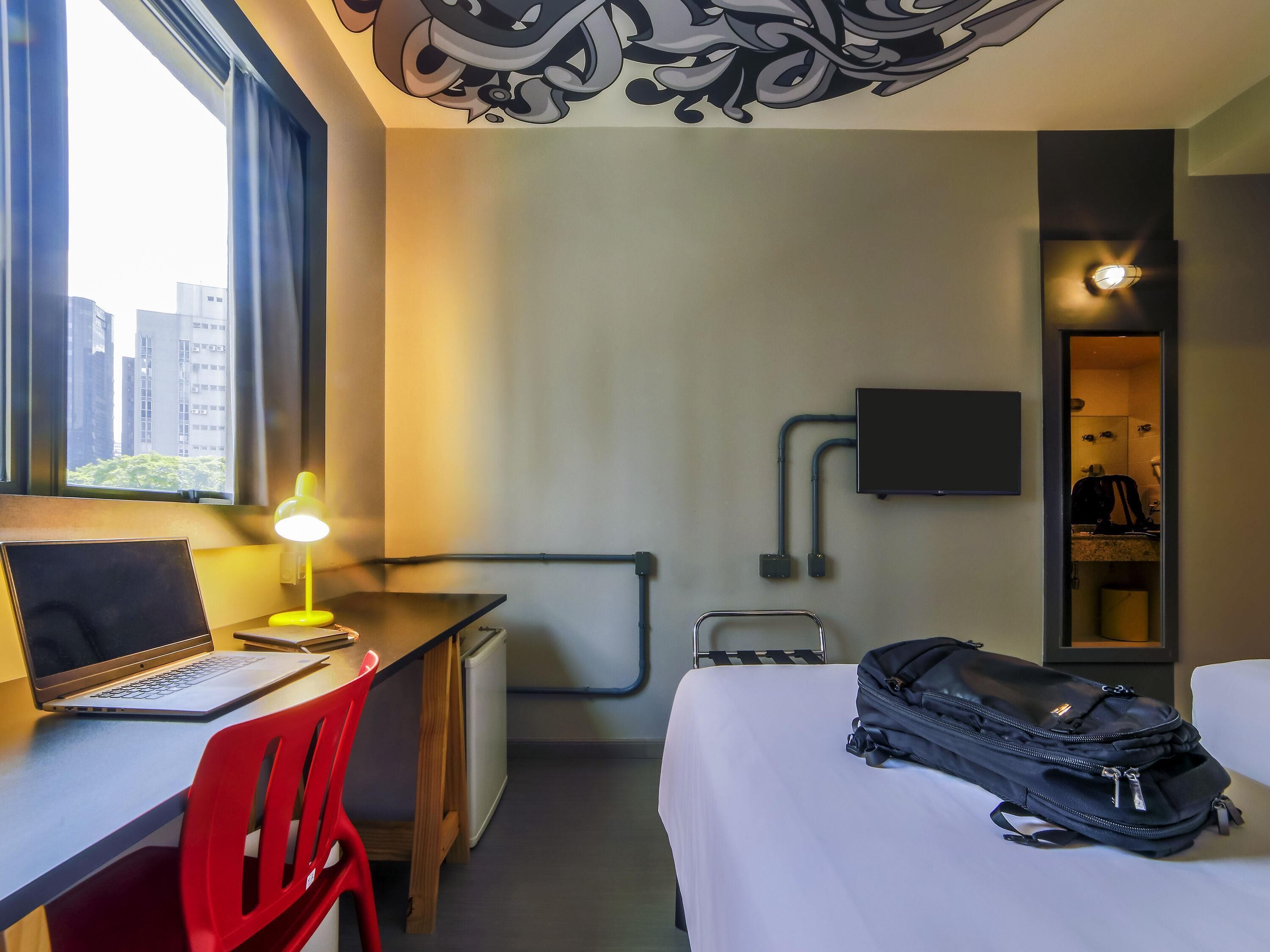 Ein Hotelzimmer mit Schreibtisch, Stuhl, Bett und Koffer.