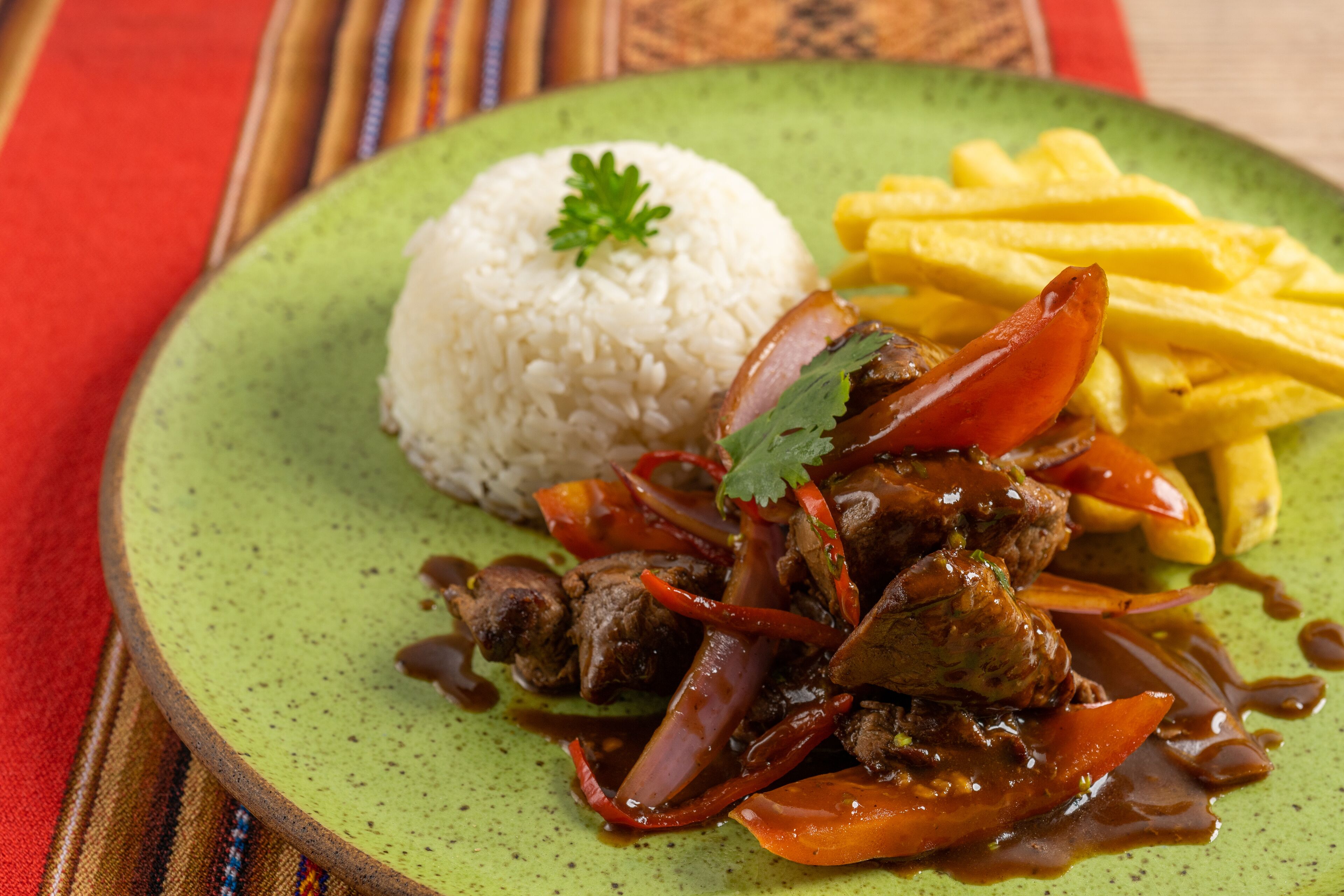 A plate with white rice, a beef dish with vegetables, and French fries.