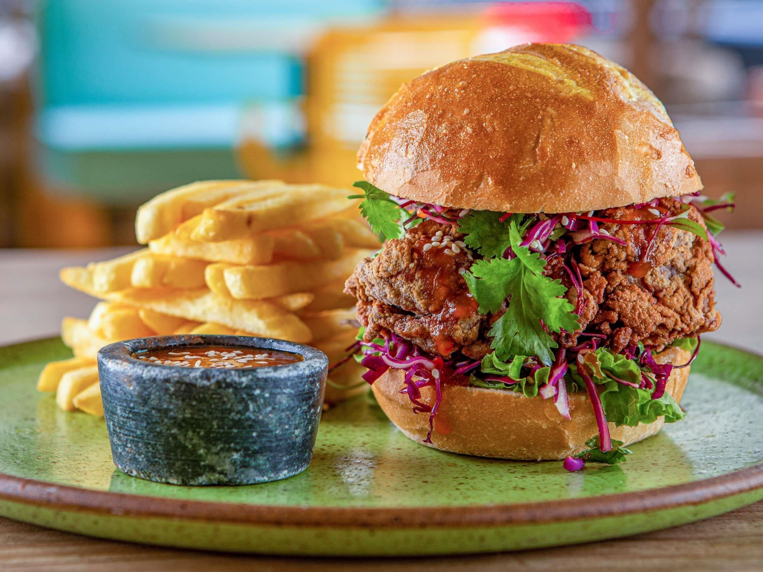 A sandwich with a side of fries and a small bowl of sauce on a green plate.