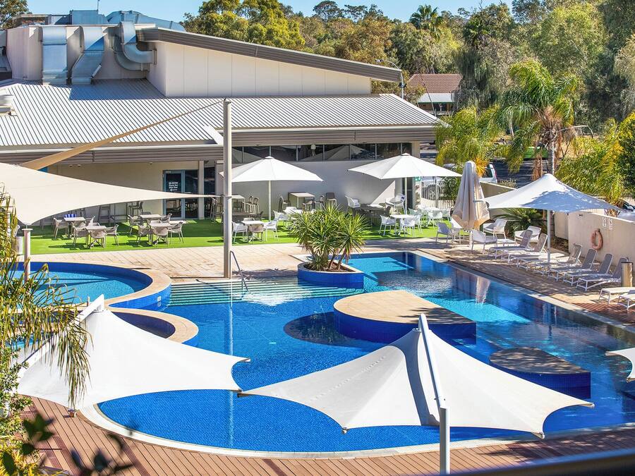 A swimming pool with multiple sections and sun loungers, surrounded by umbrellas and outdoor seating.