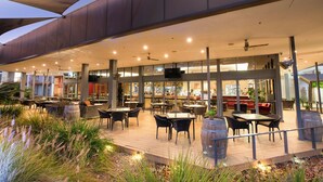 An outdoor dining area with tables and chairs, a covered seating area, and a view of the restaurant interior. - Crowne Plaza Alice Springs Lasseters by IHG (Desert Springs)