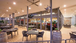 An indoor dining area with tables and chairs, a bar area, and a view of the kitchen through glass doors. - Crowne Plaza Alice Springs Lasseters by IHG (Desert Springs)