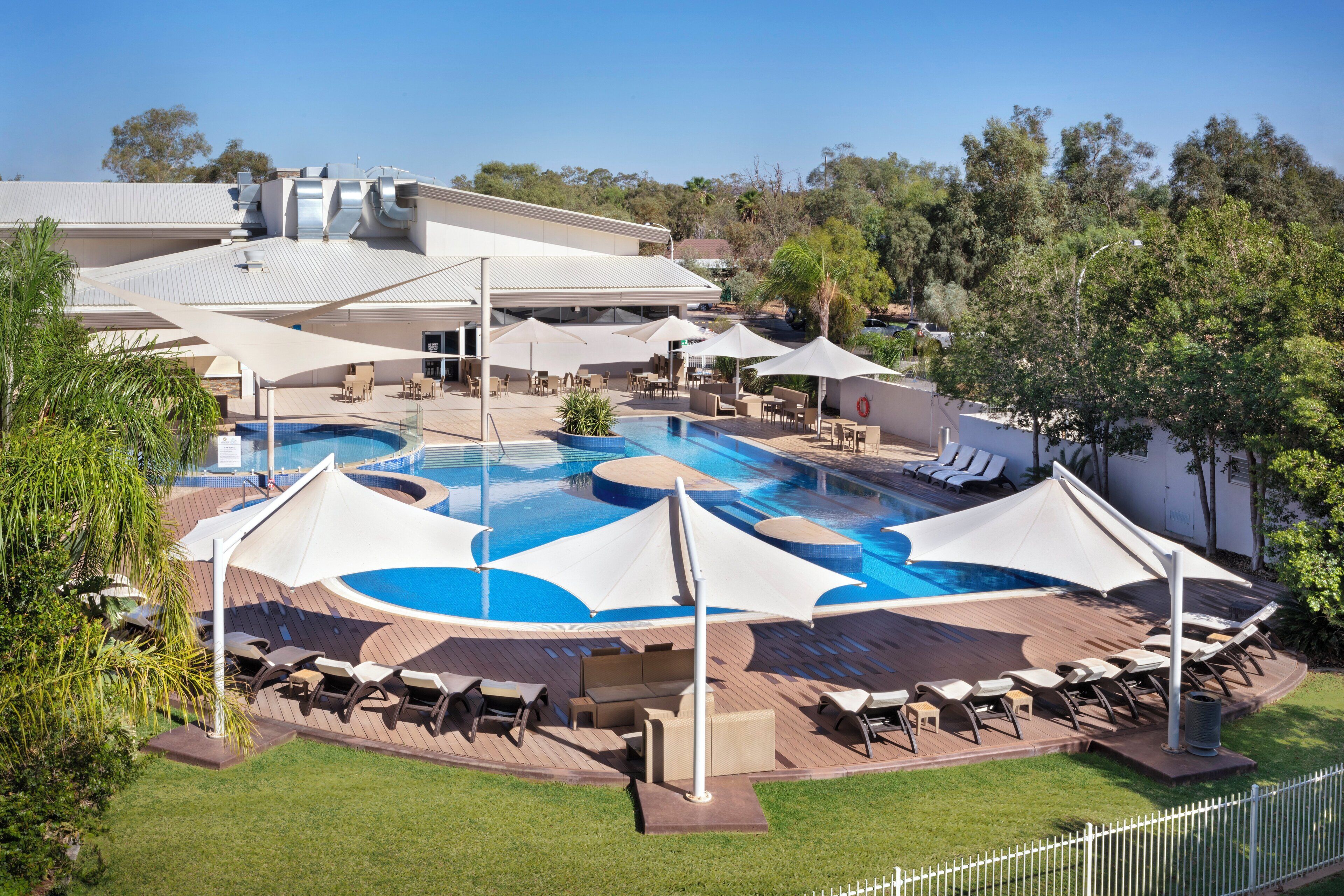 A pool area with lounge chairs and umbrellas, surrounded by a fence and greenery.