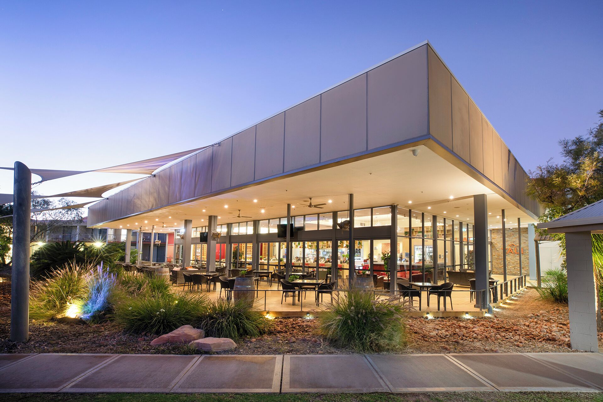 A modern building with a covered outdoor seating area, large windows, and a well-maintained garden.