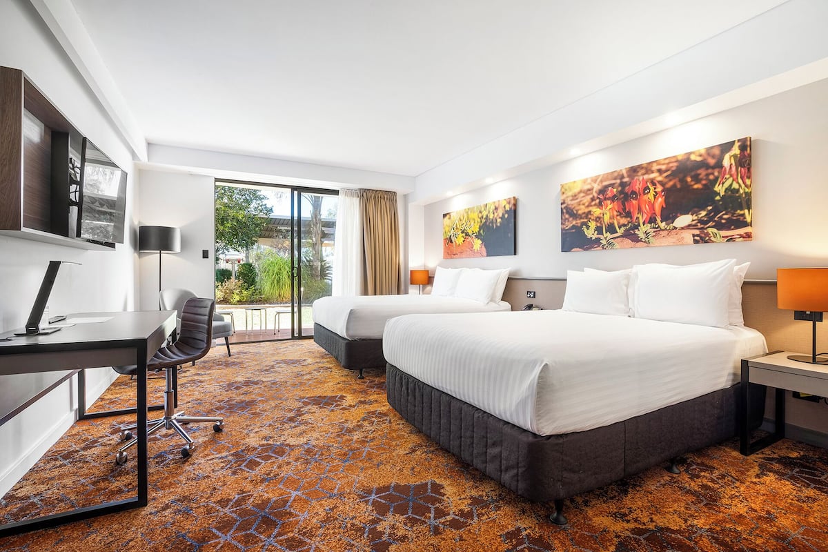 A hotel room with two beds, a desk, a chair, and a large window.