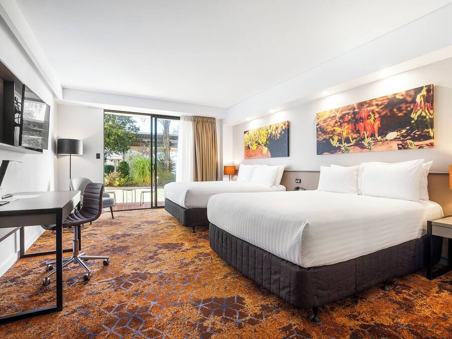 Habitación de hotel con dos camas, un escritorio, una silla y un ventanal grande.