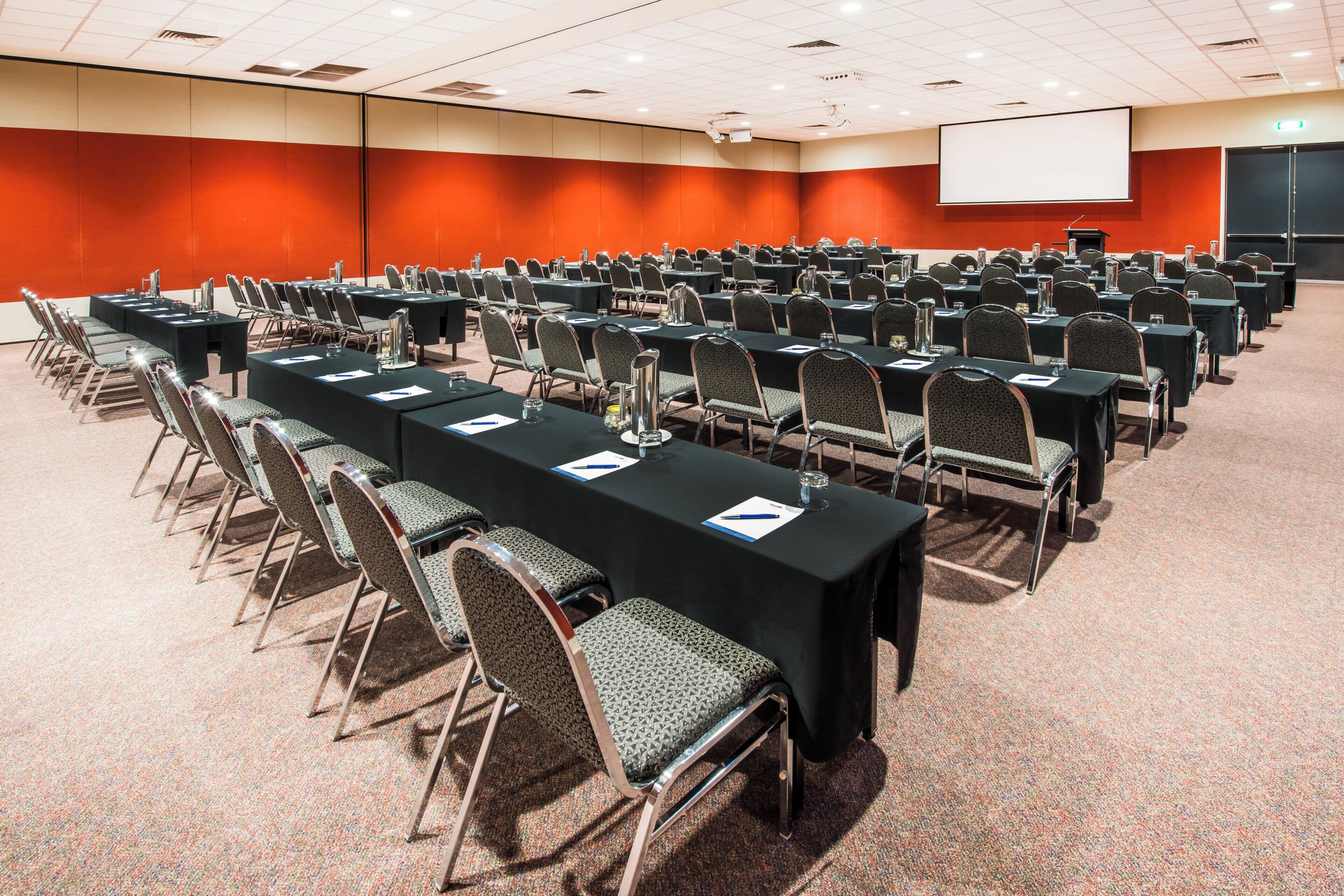 Un salón de conferencias con filas de mesas y sillas, equipado con tarjetas de identificación y botellas de agua.
