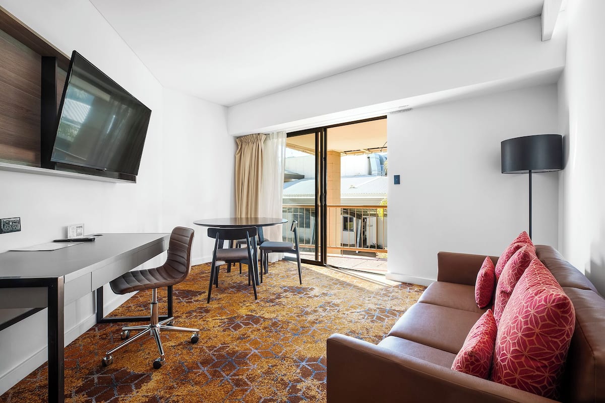 A hotel room with a dining area, a sofa, a TV, and a balcony with a view.