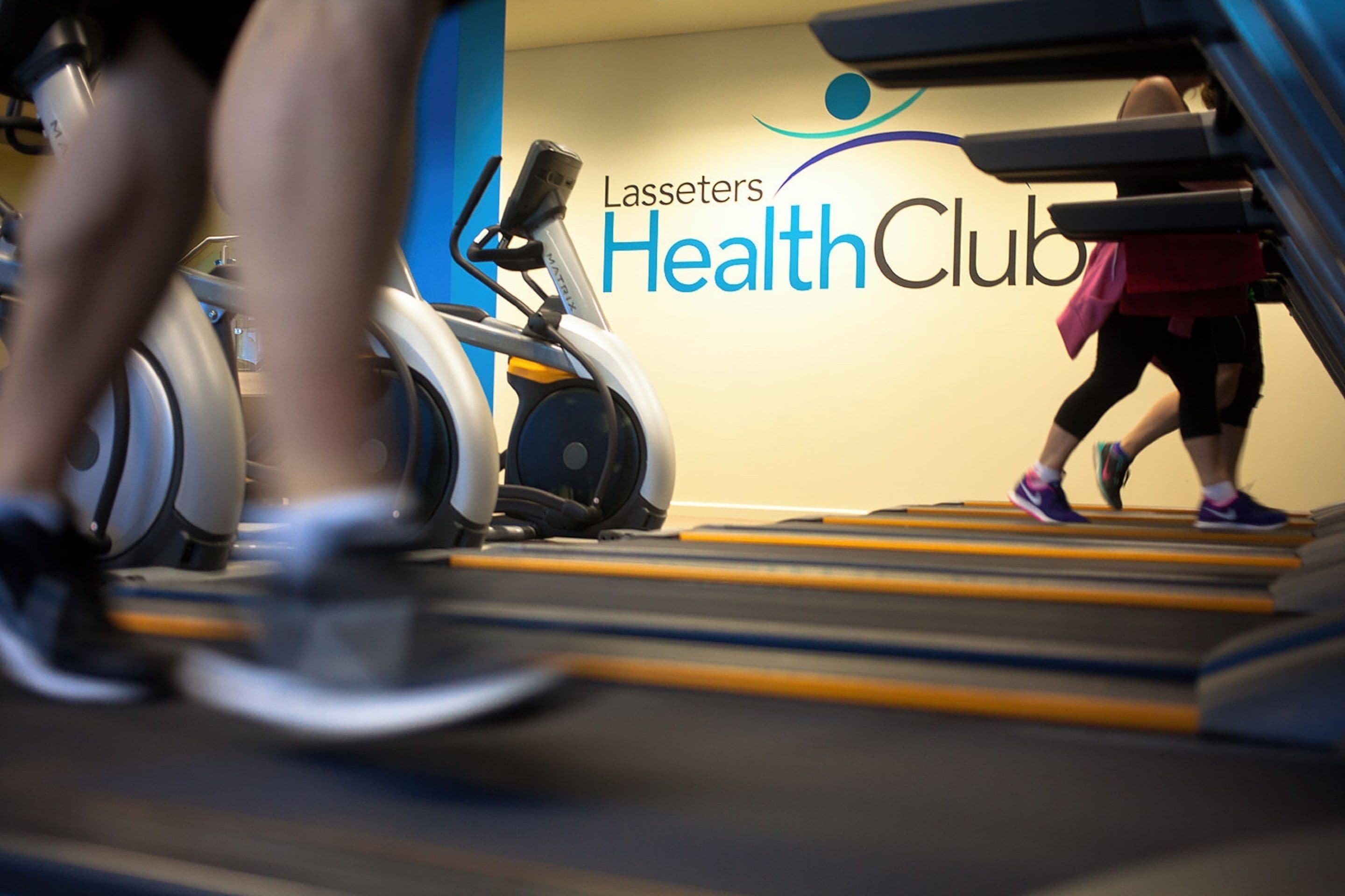 A treadmill in a gym with a sign that reads "Lasseters Health Club".